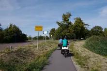 Das Bild zeigt zwei Radfahrende vor dem Ortsschild "Wörlitz" in Rückenansicht