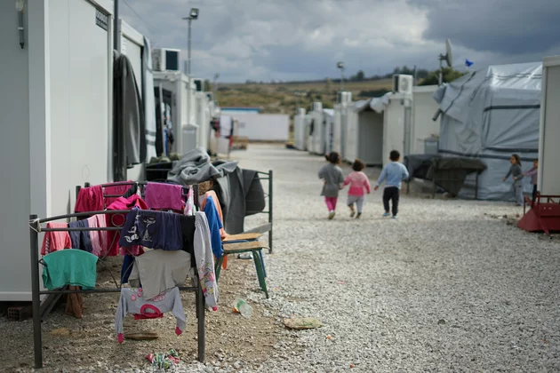 Das Bild zeigt ein Geflüchtetencamp und im HIntergrund drei Kinder.