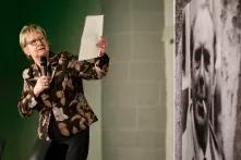 Sylvia Lörhamnn auf einer Bühne vor einem Bild von Heinrich Böll, sie hält ein Blatt Papier hoch und spricht in ein Mikrofon.