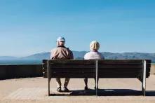 Zwei Senior*innen von hinten auf einer Bank fotografiert, dahinter Aussicht über blauen Himmel.