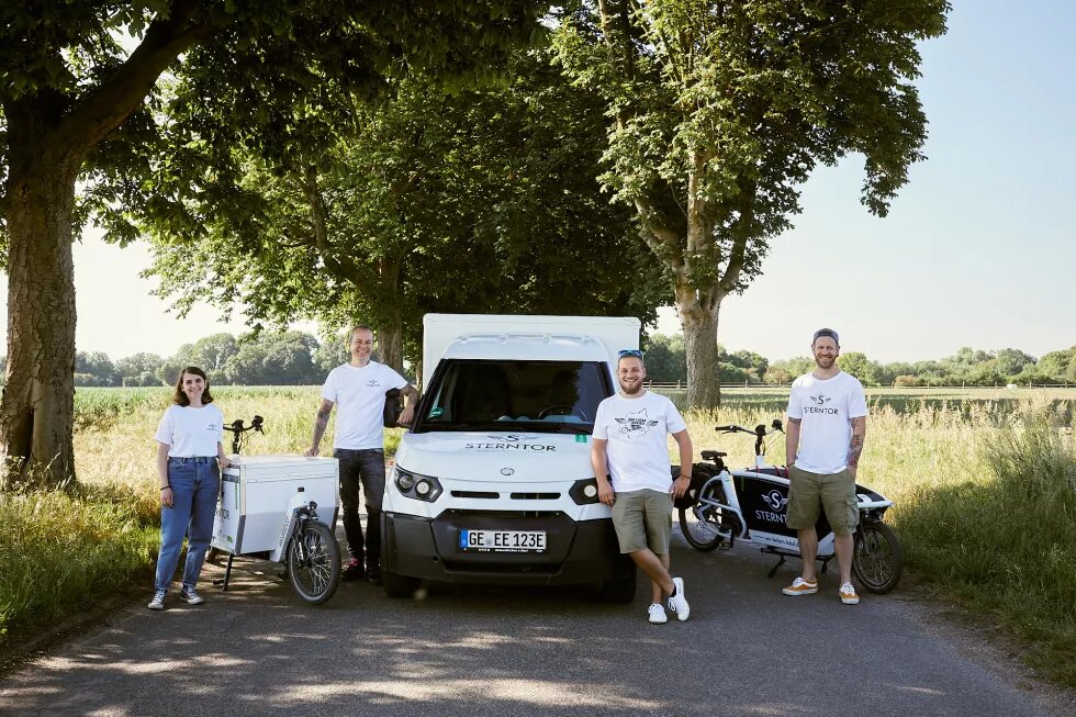 Vier Menschen in weißen Shirts, ein E-Laster und ein Lastenrad.