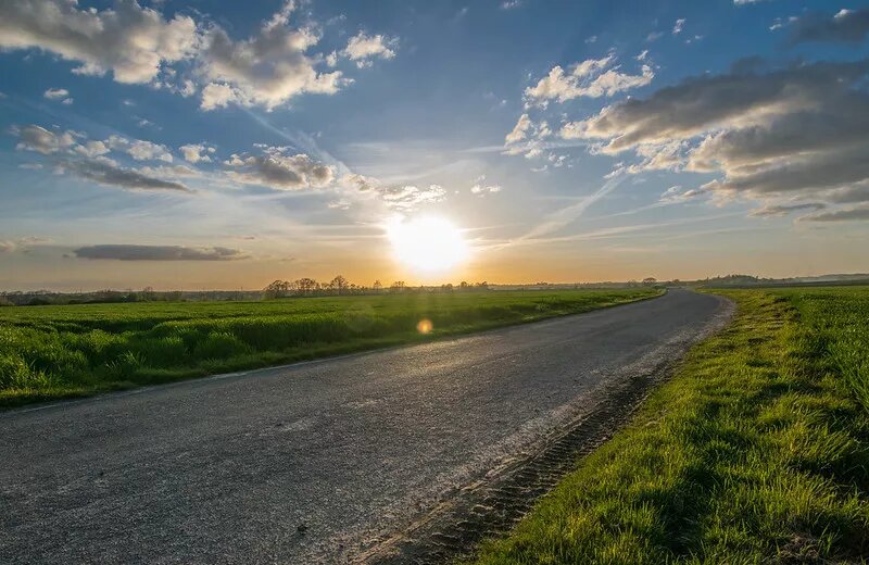 Das Bild zeigt den Sonnenuntergang über einem asphaltierten Weg.